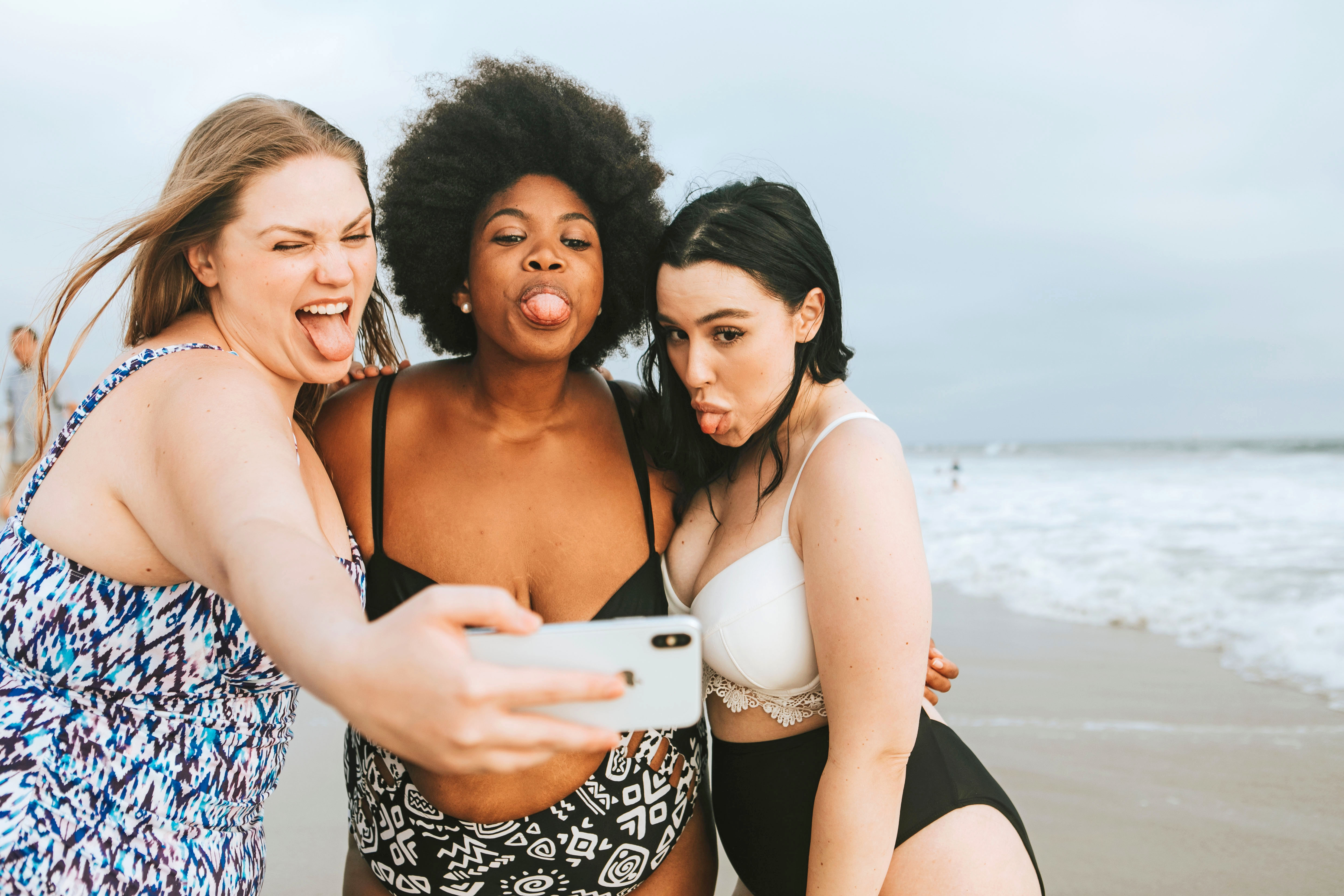Drei vollschlanke Teenager im Badeanzug schneiden Grimassen beim Selfie am Strand